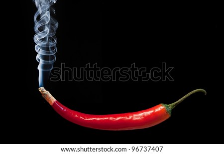 Red hot chili pepper with smoke coming out of tip which is burning and glowing