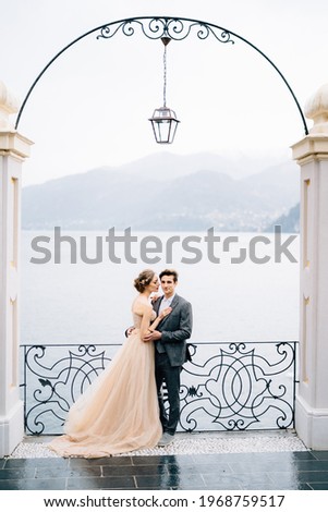 Newlyweds hug and almost kiss under an old arch against the backdrop of Lake Como Foto stock © 
