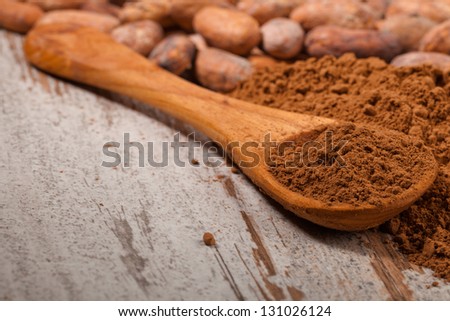 cacao beans and cacao powder in spoon over wooden background