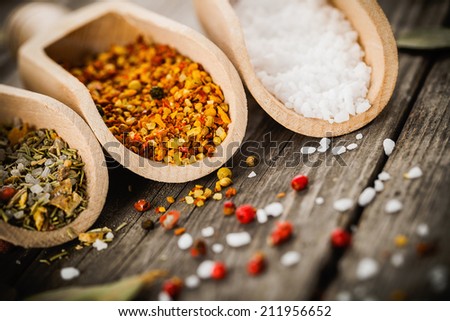mixed spices for fish and chicken cooking and salt in wooden scoops, bay leaves and pepper corns on old vintage table