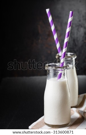 Two bottles with milk on dark background with purple striped straws