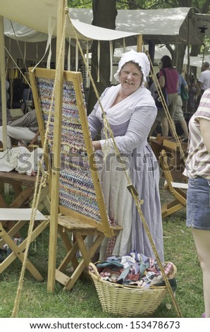 WHEATON, ILLINOIS/USA - SEPTEMBER 7: American Revolutionary War (1775-1783) reenactment on September 7, 2013, in Wheaton, IL. Woman actor in period dress demonstrates weaving at wooden frame by tent.