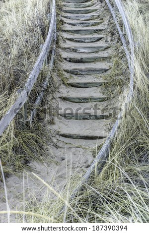 Wooden steps, partly covered with sand, with curved wooden railing at the bottom of a steep but stable dune by Lake Michigan early in spring