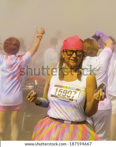 KALAMAZOO, MICHIGAN, USA - April 12, 2014: A woman runner holds a mobile phone in one hand and a packet of colored powder in the other as the crowd around her celebrates \