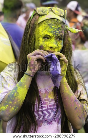 LAKE ZURICH, ILLINOIS, USA - June 20, 2015: Vividly powdered on her face and arms, a young woman participant uses her teeth to open a bag of blue powder after a 5K \