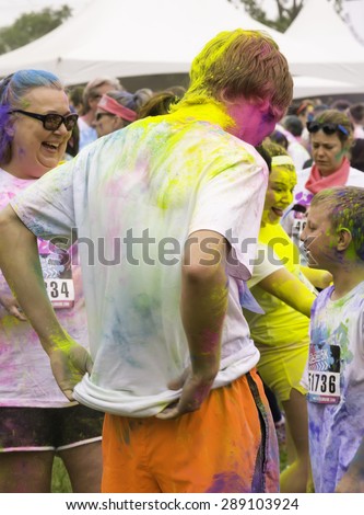 LAKE ZURICH, ILLINOIS, USA - June 20, 2015: A teenaged boy with colored powder dumped on him checks his T-shirt near a woman laughing before a 5K \