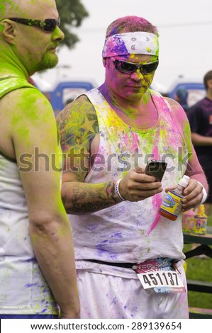 LAKE ZURICH, ILLINOIS, USA - June 20, 2015: A man doused in colored powder checks his cell phone while another participant and he await the start of a 5K \