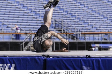 PARK RIDGE, ILLINOIS, USA - July 23, 2015: A senior high jumper lands safely on a crash mat during a track and field event in the Six-County Senior Games on a summer morning in suburban Chicago.