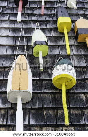 Painted wooden buoys, once used for lobster traps, hanging on exterior wall covered with weathered cedar shakes in Maine