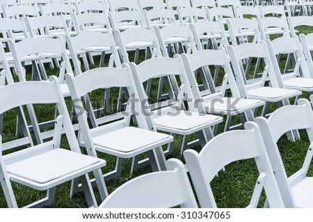 Symmetry of love: Rows of white folding chairs on lawn before a wedding ceremony in summer