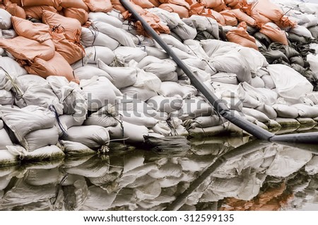 Wall of sandbags and pump discharge tube reflected by puddle in parking lot near the Illinois River: Documentary detail for themes of flood control, emergency response, preparedness