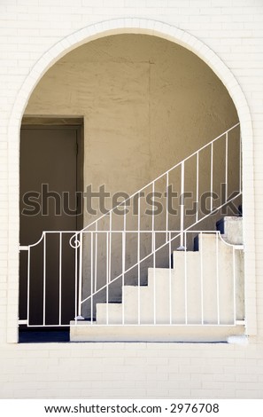 Arch and recessed door, guardrails, and stairway at side of white brick building in southwestern United States