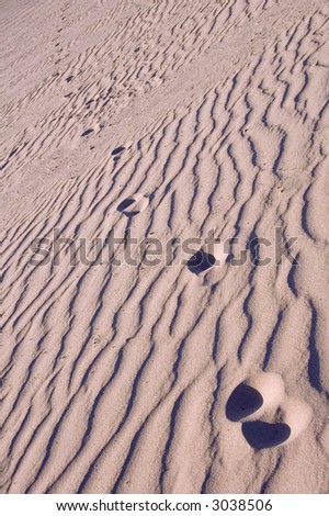 Human footprints in rippled sand, shadowed by sinking sun, diminish with distance - tilted view