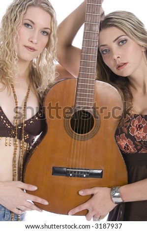 Two sexy young Caucasian women stand holding a guitar between them, isolated on white background