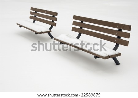 Two snow-covered benches by a tennis court under snow
