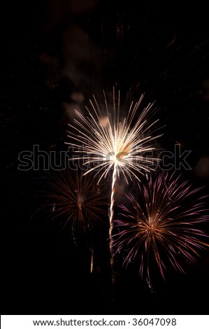 Bright white fireworks burst by multicolored embers from previous explosion