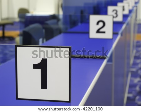Black and white number signs along blue registration counter in convention hall (focus on 1)