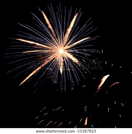 Intense burst of fireworks with feathery motion blur and blue streaks above embers from previous burst