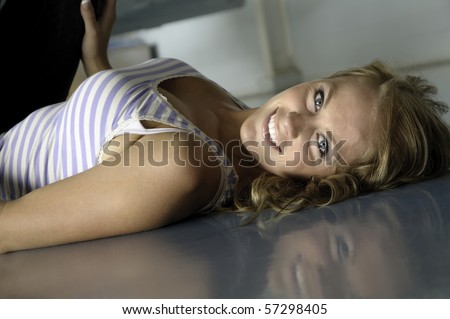 Smiling young Caucasian woman lies on reflective floor of hangar, hand on airplane wheel