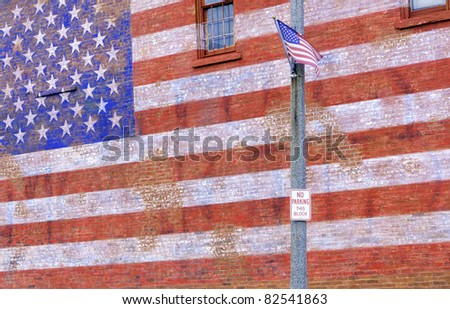 Small-town street scene in Illinois: American flag flapping in breeze by huge painted American flag fading from brick wall
