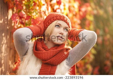 beautiful blond woman in red knitted scarf hat and gloves posing against colorful grape leaves