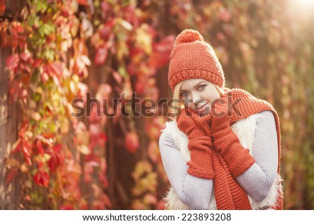 beautiful blond woman in red knitted scarf hat and gloves posing against colorful grape leaves