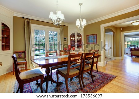Elegant big dining room with khaki walls, hardwood floor, cherry wooden dining table set, and rustic cabinets