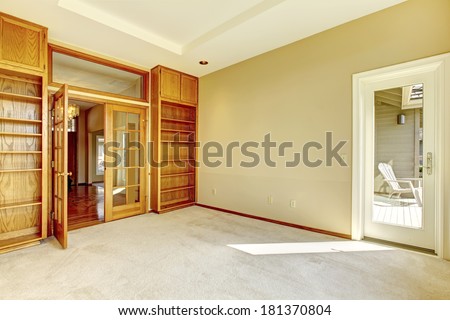 Empty room with carpet floor and ivory wall. View of bookshelves and french open door