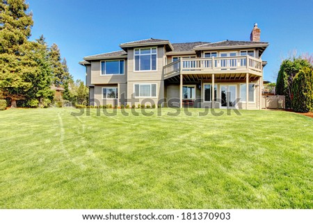 Clapboard siding house with walkout deck. View of back yard with green lawn and fir trees