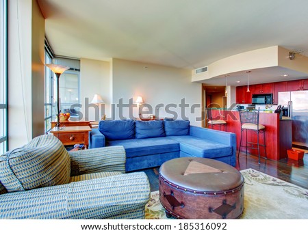 Living room with blue sofa, striped armchair and leather ottoman. View of beautiful bright color kitchen room
