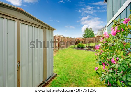 Fenced backyard with green lawn with blooming flowers. View of shed