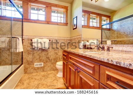 Small bathroom with wooden cabinet and glass door bath tub.