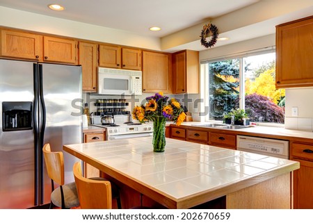 Cozy kitchen with honey color cabinets, white appliances and kitchen island with fresh flowers