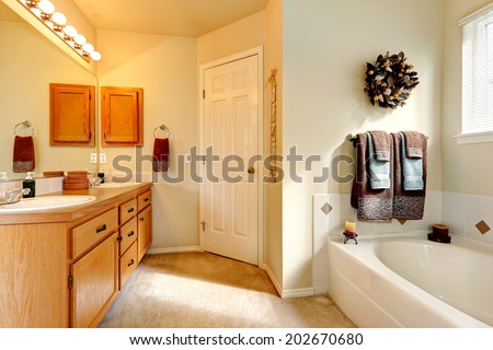 Soft ivory bathroom with carpet floor and white bath tub. View of honey bathroom vanity cabinet with mirror