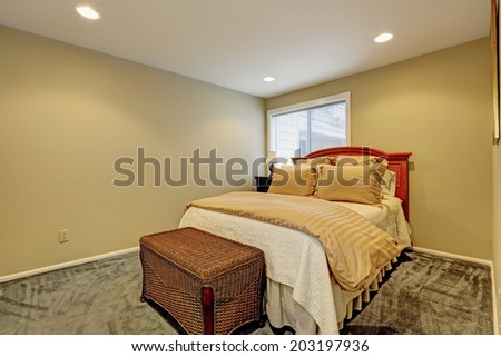 Small bedroom with dark green carpet floor, one bed and wicker ottoman