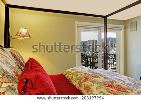 Bedroom interior with high pole bed and walkout deck. View of colorful and red bedding