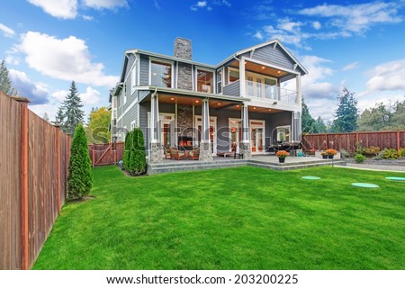 Luxury house with backyard walkout deck and column porch. View of lawn with trees and flower pots