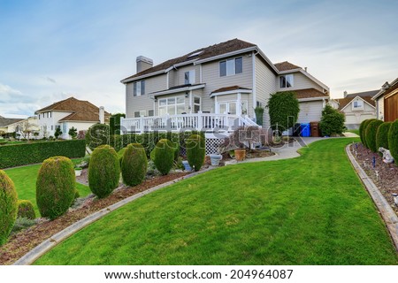 Luxury house backyard with white walkout deck, green lawn and trimmed hedges