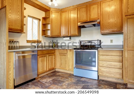 Kitchen room interior with brown tile floor, honey tone storage combination with steel appliances