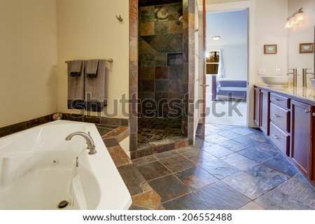 Bathroom interior with dark tile floor and tile shower trim. View of bathroom vanity cabinet with white vessel sink and white whirlpool tub