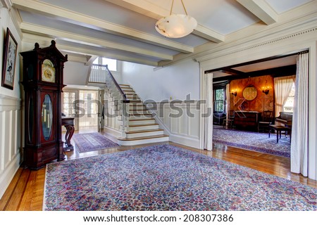 Big luxury house. Entrance hallway with blue rug, grandfather clock and staircase view