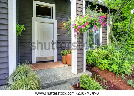 House exterior. Entrance porch with white door. Porch decorated with flower pots and blooming flowers in hanging pot