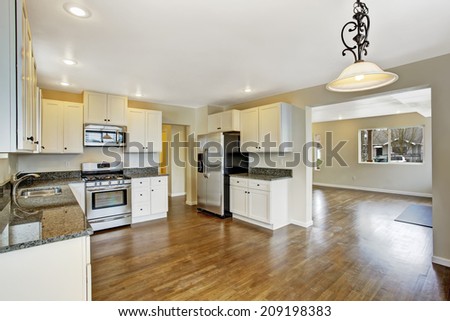 Interior in empty house with open floor plan. Spacious kitchen room with white cabinets and granite tops