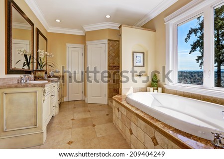 Soft tones bathroom interior with tile floor and tile wall trim, antique vanity with mirror and round bath tub in luxury house