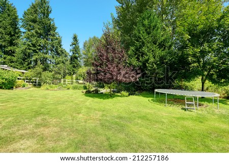 Green fenced backyard with trampoline. Countryside landscape during summer time
