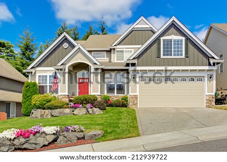 Grey house exterior with entrance porch and red door. Beautiful front yard landscape with vivid flower and stones
