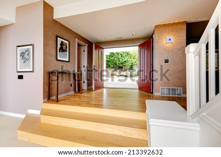 Entrance hallway in soft mocha color, with hardwood floor, stairs and red entrance door