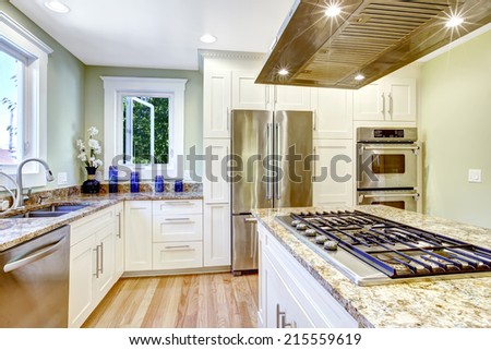 Modern and practical kitchen room design. White cabinet with granite tops and steel appliances, kitchen island with built-in stove and steel hood