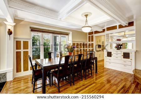 Luxury spacious dining room with hardwood floor, wood wall trim and coffered ceiling. Room in brown and white tones