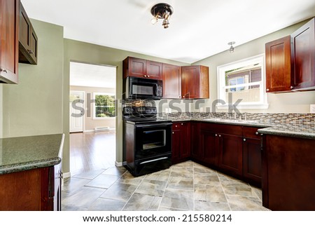Kitchen with bright burgundy cabinets and black appliances. Light mint walls and tile floor